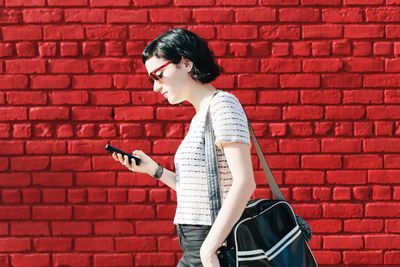 Frau vor roter Mauer blickt auf Smartphone .jpg KI-generiertes Bild