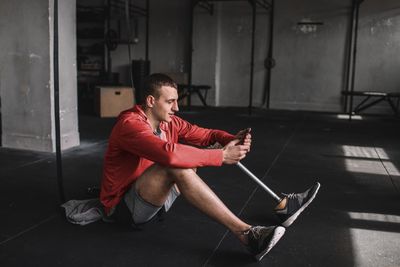 Mann sitzt im Fitnessstudio auf dem Boden und blickt auf Smartphone.jpg KI-generiertes Bild