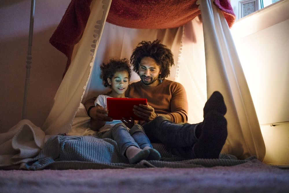 Eltern sitzen mit Kind auf dem Boden und blicken auf Tablet.jpg